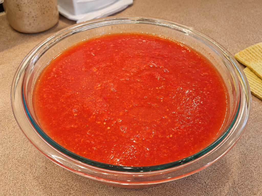 Large clear glass bowl filled with fresh red heirloom tomato purée after processing the tomatoes through a hand-crank strainer.