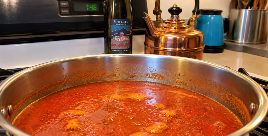 Homemade marinara sauce simmering in a stainless steel pot with a bottle of Sutcliffe Vineyards Gewürztraminer wine in the background.
